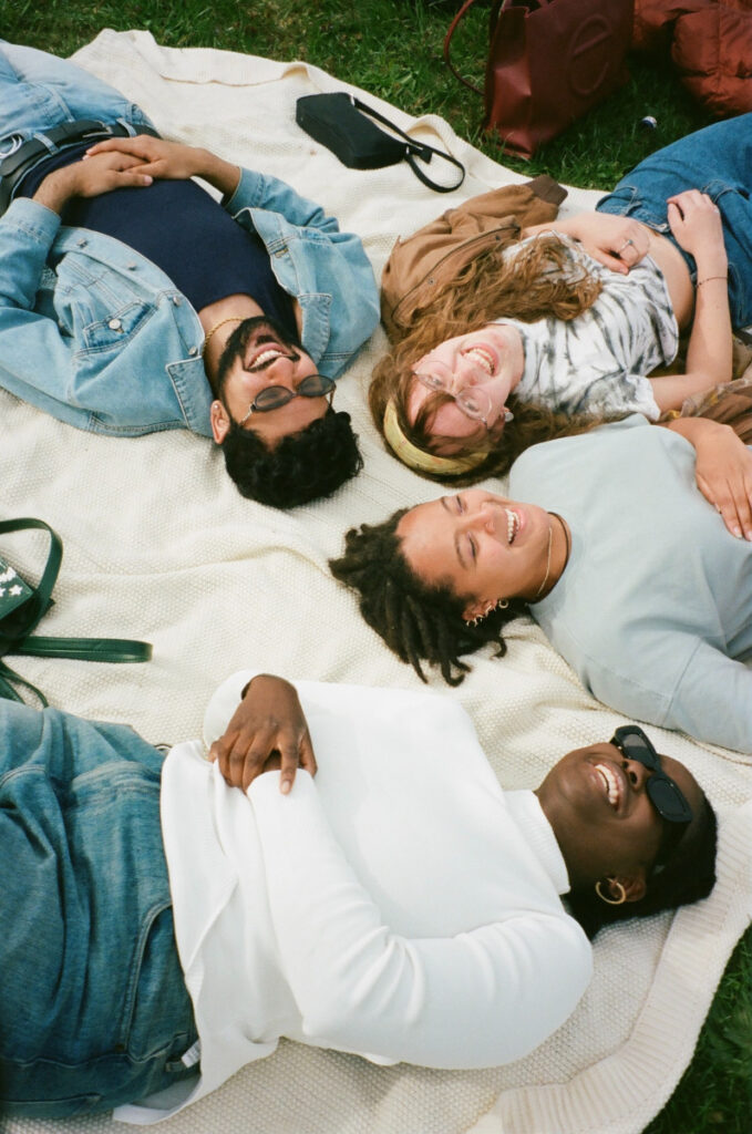 Four friends laughing on a blanket in the grass